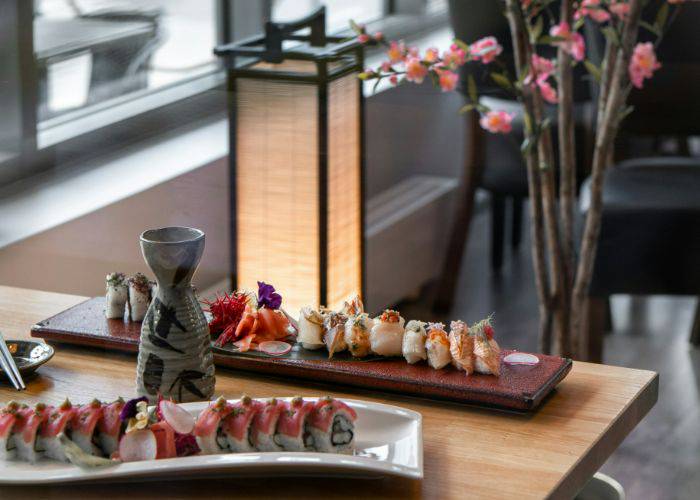 Two serving trays of fresh sushi with a bottle of sake in the middle. Behind them, a cherry blossom tree.